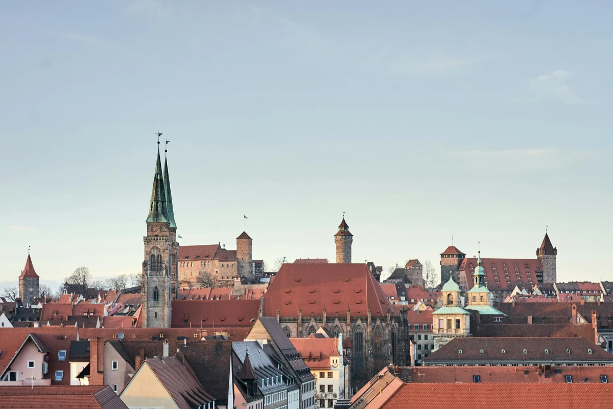 Historische Stadtsilhouette von N&uuml;rnberg mit mittelalterlichen T&uuml;rmen, Kirchen und dicht aneinander gebauten roten Ziegeld&auml;chern. Blick &uuml;ber die Altstadt mit charakteristischer Architektur und markanten Geb&auml;uden vor einem klaren Himmel.