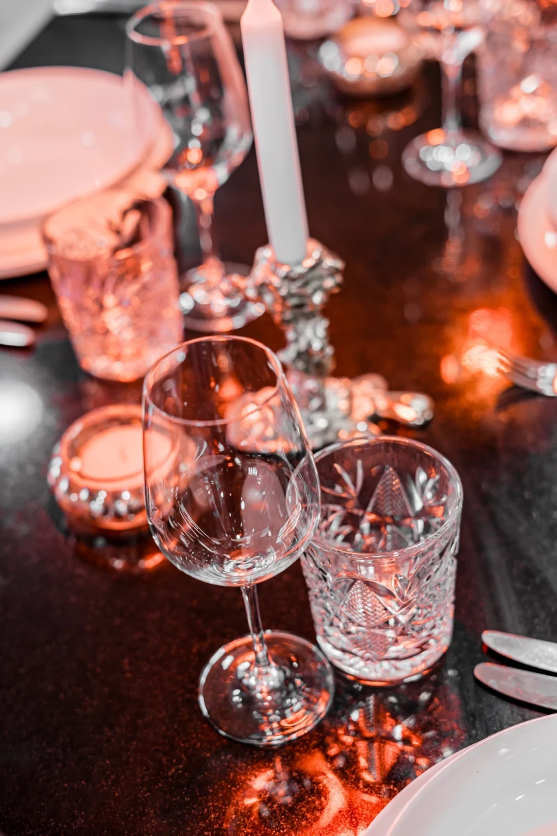 Elegante Bar-Tischszene mit geschliffenen Kristallgl&auml;sern, einem Weinglas und einem Whiskyglas. Warmes Licht und gl&auml;nzende Oberfl&auml;chen schaffen eine ged&auml;mpfte, luxuri&ouml;se Atmosph&auml;re mit r&ouml;tlichen Reflexen.