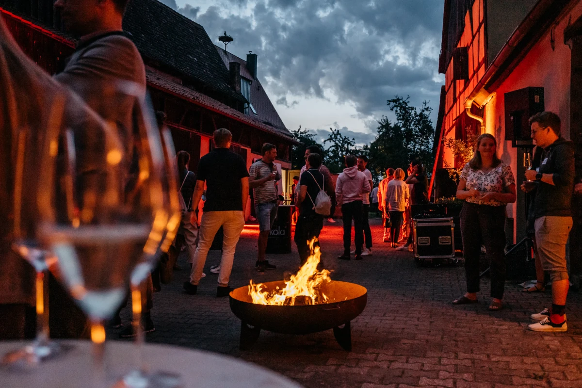 Gemütliche Abendveranstaltung am Gutshof Neun mit Feuerschale und fröhlichen Gästen.