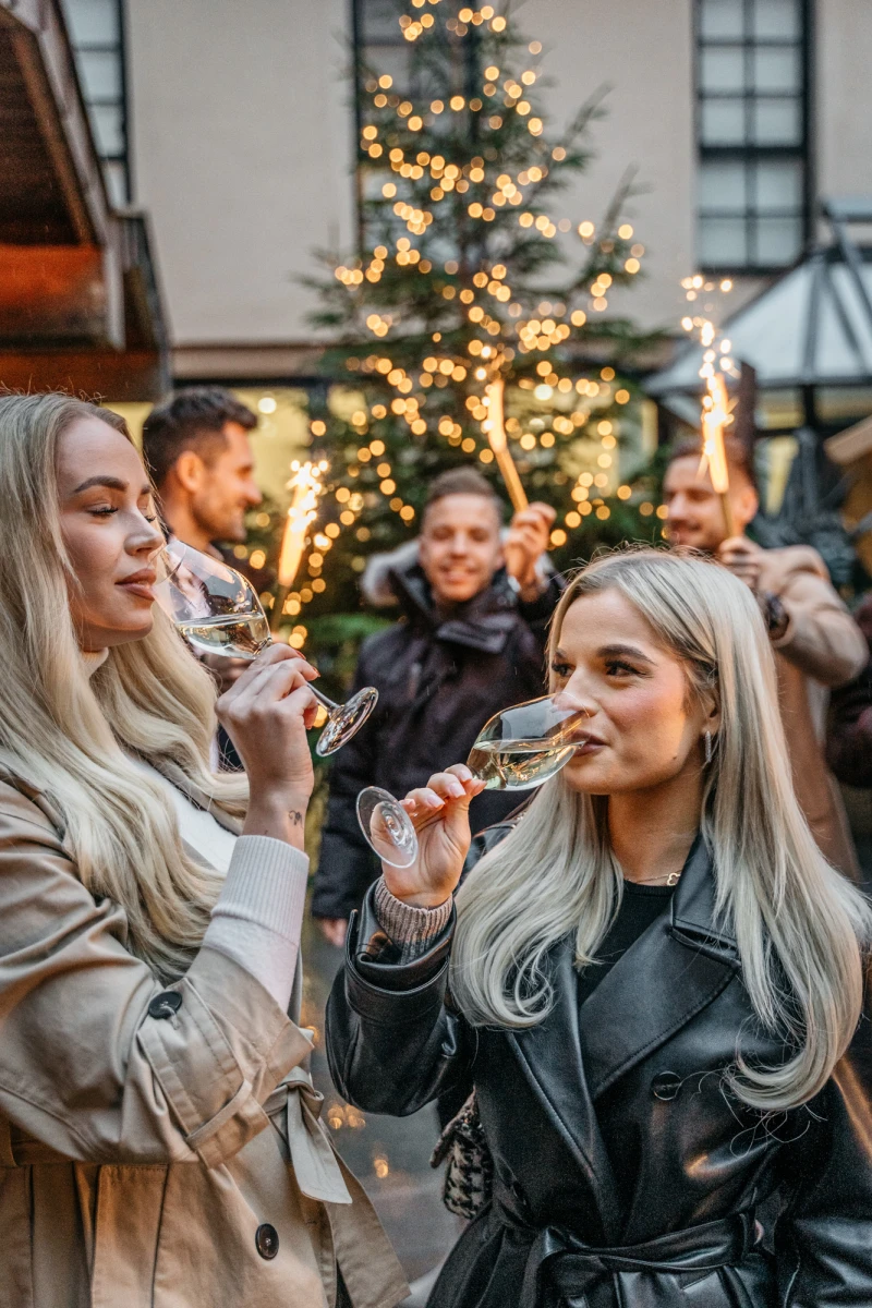 Zwei Frauen sto&szlig;en mit Gl&auml;sern an, umgeben von weihnachtlicher Dekoration im Festgarten.