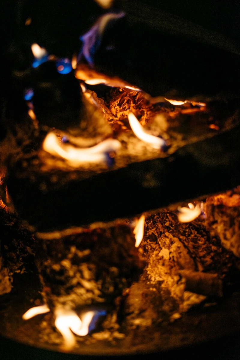Loderndes Lagerfeuer mit blauen und gelben Flammen, die &uuml;ber dunkle Holzscheite tanzen. Warme, flackernde Lichter erhellen die Dunkelheit mit einer gem&uuml;tlichen, w&auml;rmenden Atmosph&auml;re.