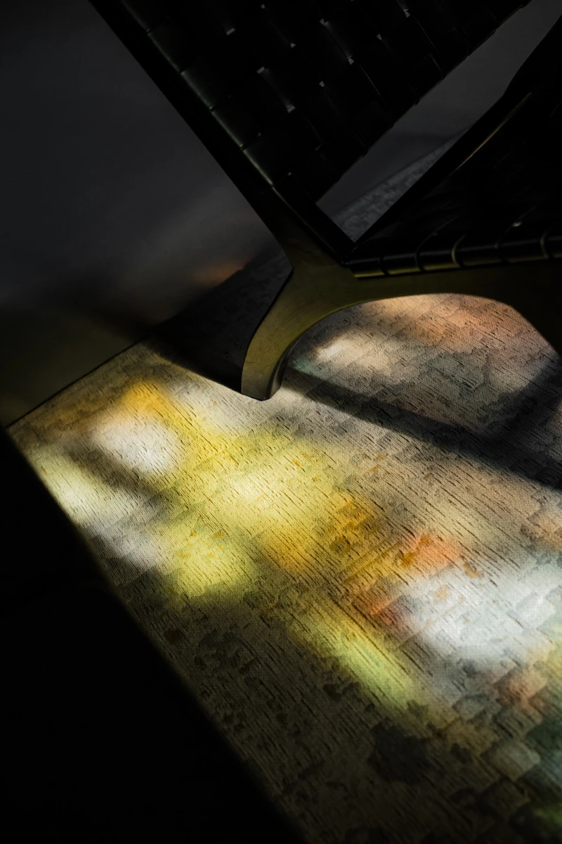 Eine ged&auml;mpfte Lichtquelle wirft gelbe und orange Lichtstrahlen auf eine alte, strukturierte Oberfl&auml;che, die wie ein Tisch oder eine Arbeitsfl&auml;che aussieht, mit einem dunklen Objektrand im Hintergrund.