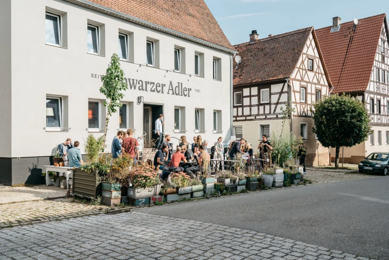 Gäste genießen sonnigen Tag vor dem historischen Gebäude des Schwarzen Adlers.