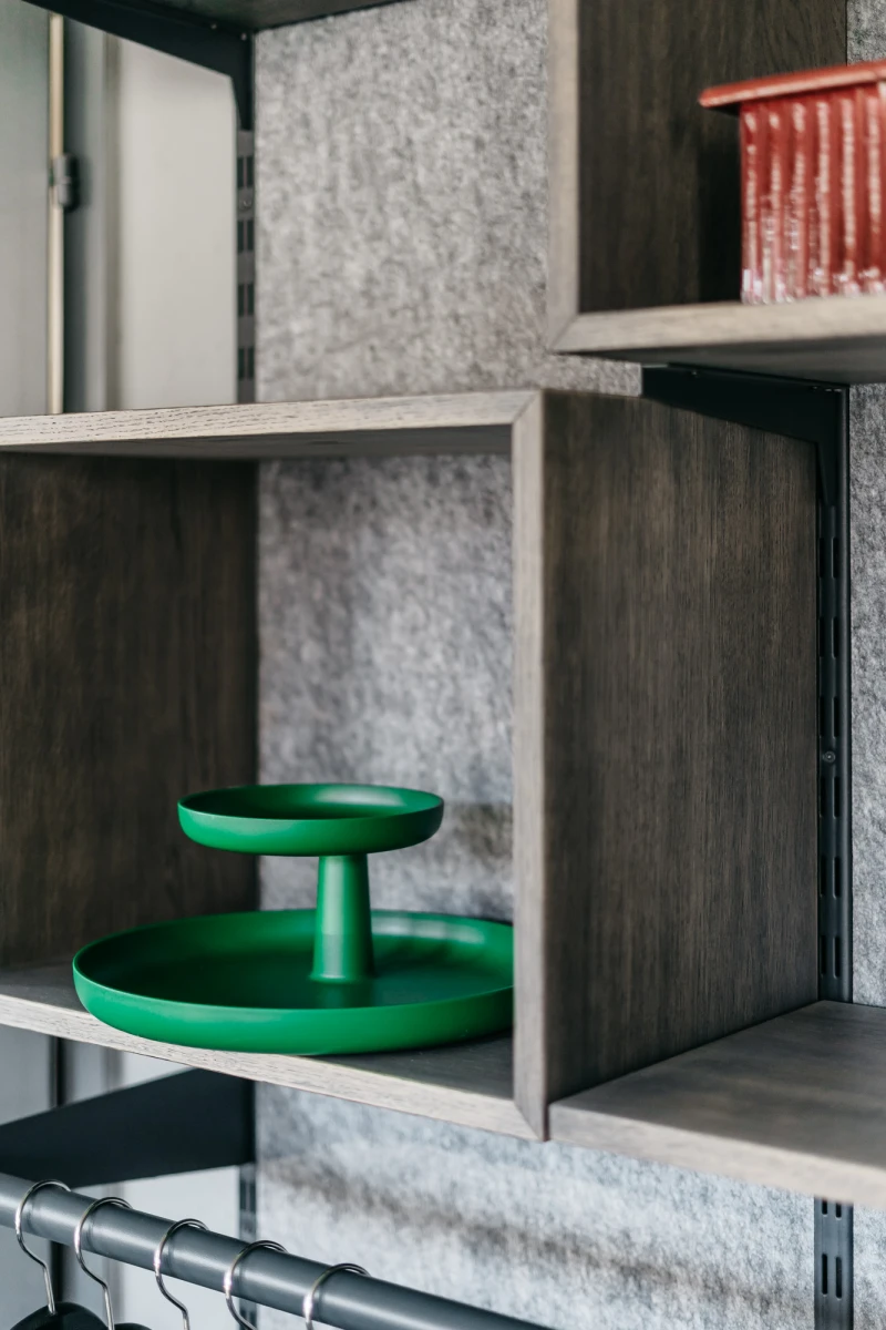 Zwei ineinandergestapelte gr&uuml;ne Schalen oder Tabletts auf einem grauen Regalfach, umgeben von Holzw&auml;nden und einem leichten grauen Hintergrundmaterial.