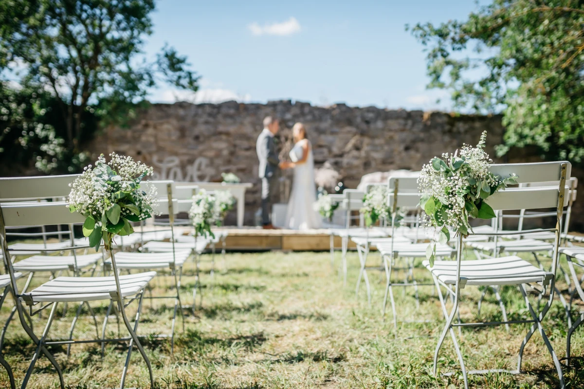 Hochzeit im Freien auf der Obstwiese im Gutshof Neun mit Blumen geschmückten Stühlen.